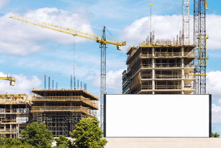 Construction site with cranes and empty advertising billboard in foregroundの写真素材