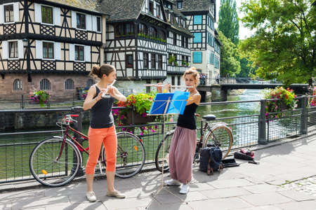 STRASBOURG, FRANCE - JULY 03, 2017: Two young adult girls playing flute in the background of fachwerk buildings in the old town of Strasbourg, Franceのeditorial素材