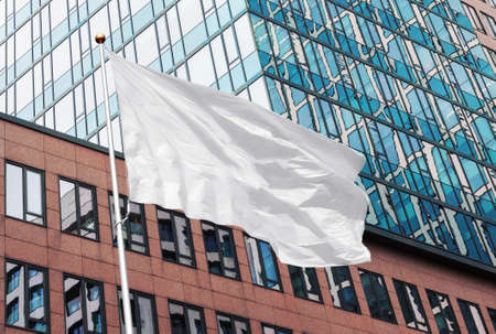 White blank flag waving in the wind in the urban background of modern buildings and skyscrapers. Perfect mockup to add any logo, symbol or signの写真素材