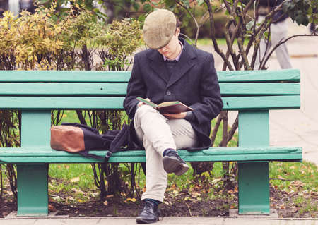 VILNIUS, LITHUANIA - OCTOBER 17,2017: Young man sitting on the bench in a park and reading a book in Vilnius, Lithuaniaのeditorial素材