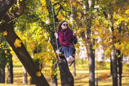 VILNIUS, LITHUANIA - OCTOBER 19,2017: Young relaxed adult girl swinging on a swing in autum park in Vilnius, Lithuaniaのeditorial素材