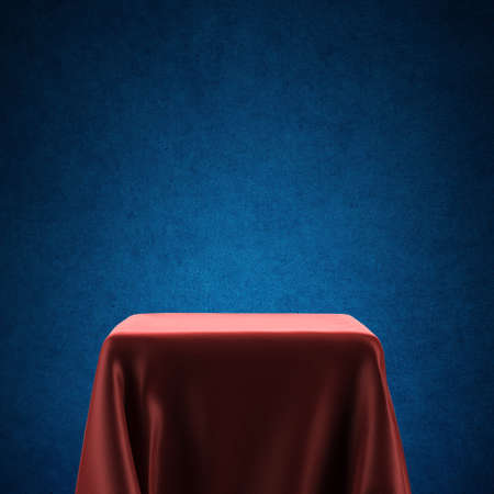 Empty spotlight pedestal covered with red cloth against blue backlit backgroundの写真素材