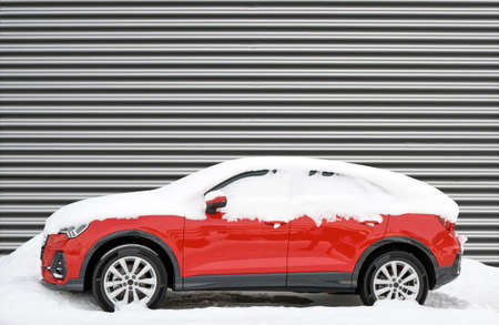 Modern red car covered in snow in winter against corrugated metal wallの写真素材