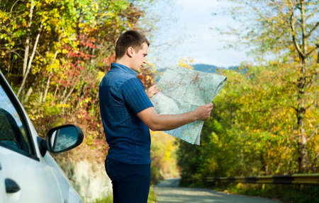 man with car in autumn road looking on travel mapの写真素材