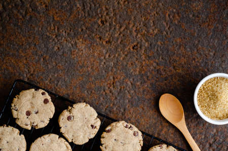 Vanilla and chocolate cookies on a black rack, a wooden spoon and muscovado sugar in a white bowl, on a dark backdrop.の写真素材