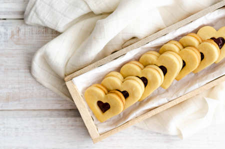 Vanilla and raspberry jam heart shaped cookies in a wooden box with a white napkin.の写真素材