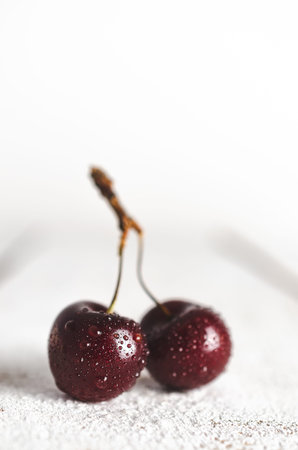 Two cherries with water drops in white wooden backdrop.