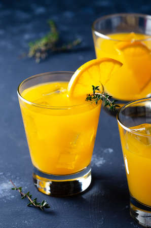 Three glasses of orange juice with thyme leaves and a slice of orange, on a blue backdrop.の写真素材