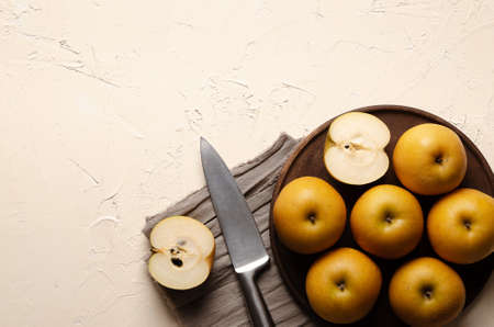 Asian pear with a silver knife on a wooden plate and a brown piece of cloth, on a light background.の写真素材