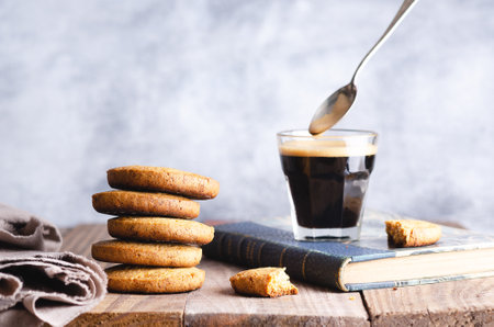 Cookies stacked and a cup of coffee on a blue book and a beige napkin on a wooden table.の写真素材