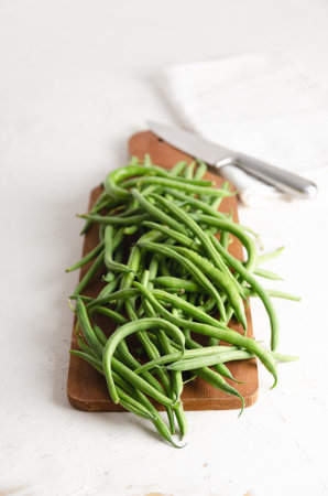 Green beans on a wooden board with a knife and a white napkin, on a white background.の写真素材