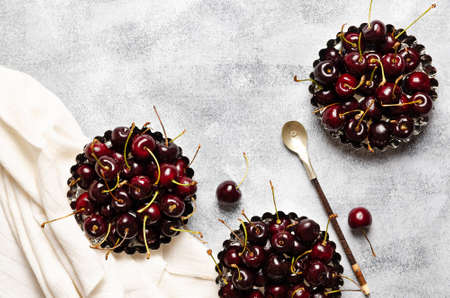 Cherries in mini baking pans with a spoon and a white napkin, on a gray background.の写真素材