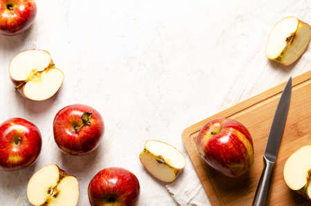 Red whole and sliced apples on a wooden board with a knife and a white napkin on a light background.の写真素材