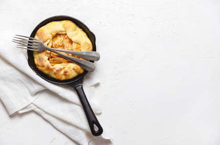Apple galette in a black pan with two forks, and a piece of white cloth on a white background.の写真素材