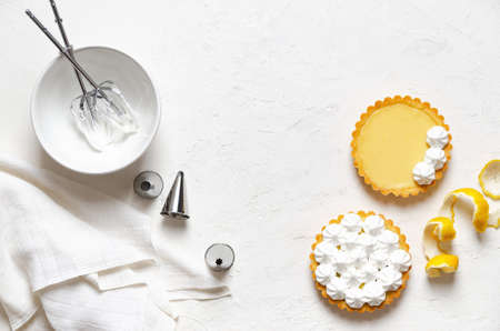 Mini lemon pies with meringue, lemon peel, whisks in meringue, piping nozzles and a white napkin, on a white background with copy space.の写真素材