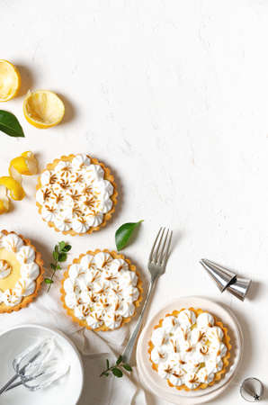 Mini lemon pies with meringue, lemon peel, lemon leaves, whisks with meringue, a fork, and some piping nozzles, on a white background with copy space.の写真素材