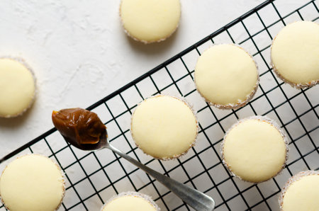 Cornstarch alfajores with coconut and a spoonful of dulce de leche on a black rack and light gray background.の写真素材