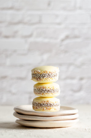 Three cornstarch alfajores with coconut on three little plates on white brick wall.の写真素材