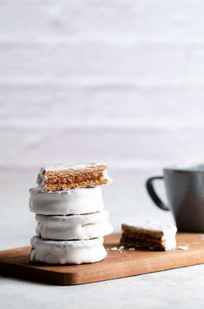 White alfajores filled with dulce de leche and a blue cup on a wooden board and white background.の写真素材