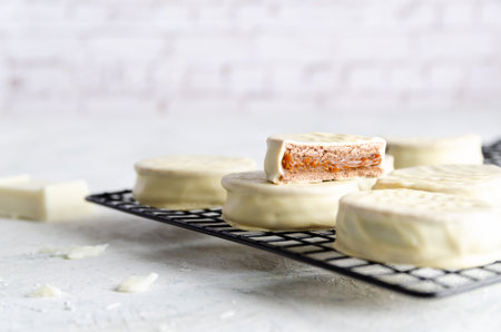White chocolate alfajores on a dark rack with a piece of white chocolate, on light background.の写真素材