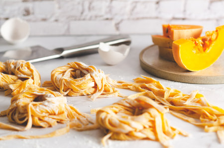Butternut squash noodle nests, some slices of butternut squash in a plate, egg shells and a knife on marble background.の写真素材