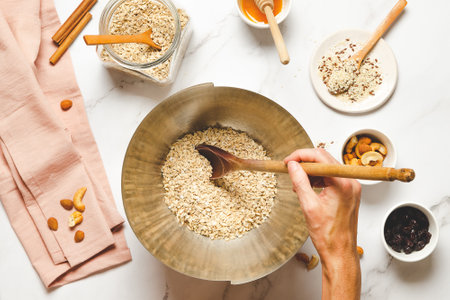 Making homemade granola. Bowl of oatmeal with nuts and honey on white marble table.の写真素材