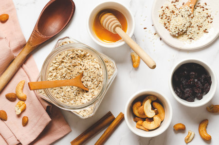 Cooking homemade granola. Oatmeal with nuts, seeds, cinnamon sticks and honey on a white marble background, top view.の写真素材