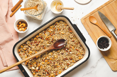 Homemade granola with nuts, dried cranberries and honey in a baking pan on a white marbled background, top view.の写真素材