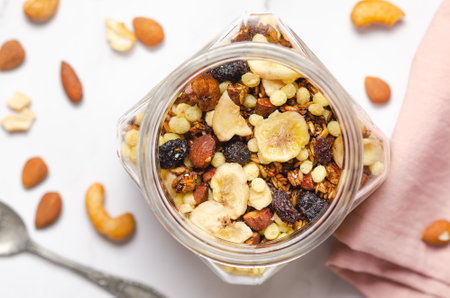 Homemade granola with dried banana slices, dried cranberries and nuts in a glass jar, top view.の写真素材