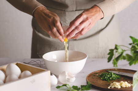 Close up of woman's hands breaking an egg into a bowl with parsley and garlic on a wooden board. The process of preparing Argentine milanesas.の写真素材