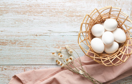 Easter eggs in a basket on a light wooden background with a pink napkin, white flowers and copy space.の写真素材