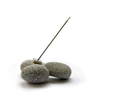 A stick of burning Japanese incense on some smooth pebblesの写真素材