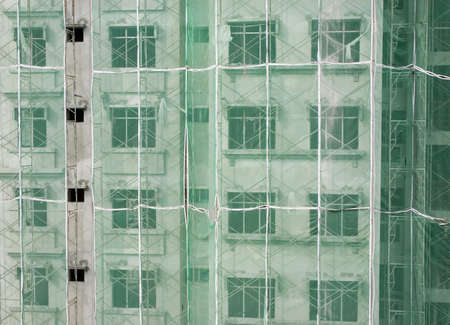 Apartment building under construction with scaffolding and green netting on its exteriorの写真素材