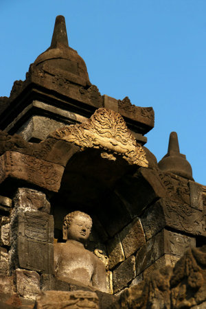 One of the many Buddha statues sitting inside an alcove in the ancient temple of Borobudur,Java,...