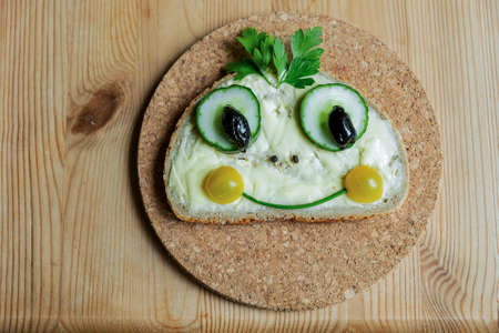 The sandwich with funny muzzles made from vegetables a half of a tomato ,cucumber slies,black olives,parsley on the cork board and wooden table.の写真素材