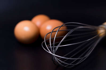 eggs and whisk isolated on black backgroundの写真素材
