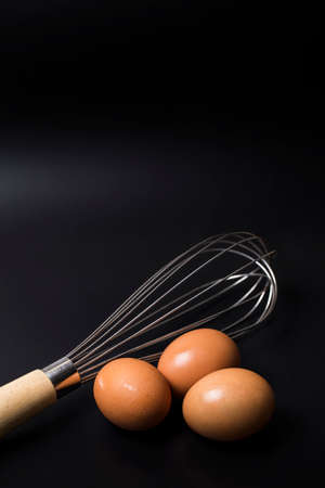 eggs and whisk isolated on black backgroundの写真素材