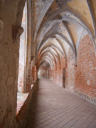 Vaulted ceiling in Gothic style with red brick walls on a historic medieval building looking down a receding empty exterior open air passageway with pavingのeditorial素材