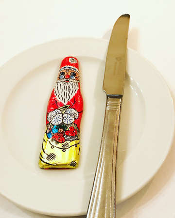 Wrapped Santa Claus chocolate sweet on plate with knifeの写真素材