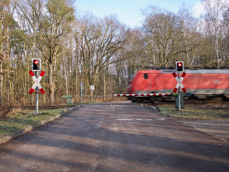 Red train speeding through a rural automated level crossing with flashing lights and the barriers...