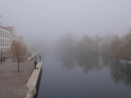 Urban fisherman or anglers fishing in a river on a cold winter day standing on the wall with rods an reels in a bleak frosty misty landscapeの写真素材