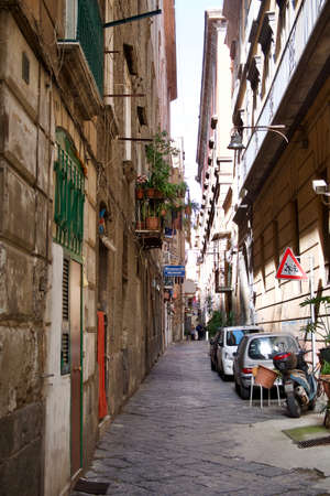 Narrow paved urban street with parked cars and motorcycle below old townhouses with a children crossing warning traffic signの写真素材