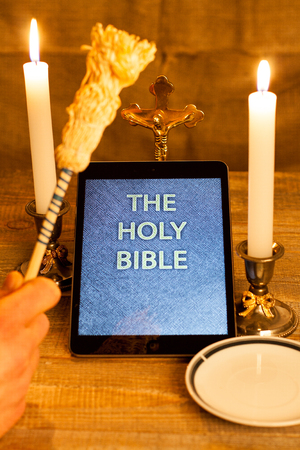 Digital  holy bible as a symbol of a new era. Scene from the cross, candles and sprinkler and hands folded in prayerの写真素材