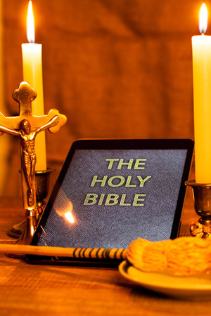 Digital  holy bible as a symbol of a new era. Scene from the cross, candles and sprinkler.