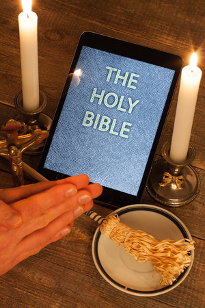 Digital  holy bible as a symbol of a new era. Scene from the cross, candles and sprinkler and hands folded in prayerの写真素材