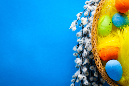 Easter Basket with easter eggs and yellow feathers and catkins on blue paper background.の写真素材