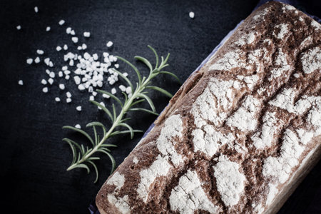 Bread, salt and rosemary lying on black stone background, top view.