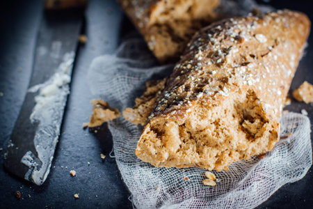 Torn baguette from dark bread with seeds and a knife smeared with butter.
