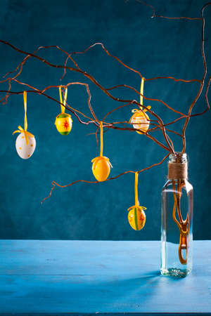 Easter eggs hanging on branch on blue background with copy space.の写真素材