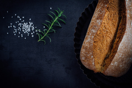 Bread, salt and rosemary lying on black stone background, top view.の写真素材
